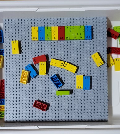 Legosteine mit Braille- und Schwarzschriftbuchstaben. Gelegt ist das Wort "Einladung"